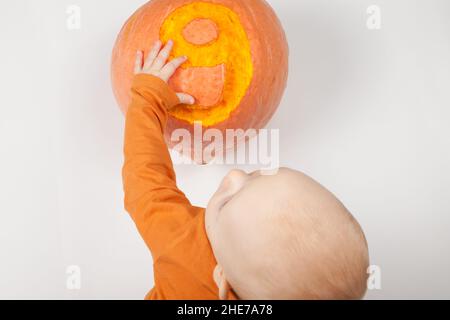 Sorridente neonato felice nove mesi bambino nei vestiti arancioni sul letto luminoso e arioso copia spazio infanzia con zucca con il numero 9 scolpito su di esso Foto Stock