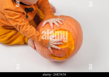 Sorridente neonato felice nove mesi bambino nei vestiti arancioni sul letto luminoso e arioso copia spazio infanzia con zucca con il numero 9 scolpito su di esso Foto Stock