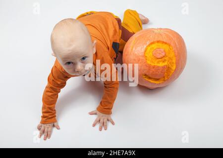 Sorridente neonato felice nove mesi bambino nei vestiti arancioni sul letto luminoso e arioso copia spazio infanzia con zucca con il numero 9 scolpito su di esso Foto Stock