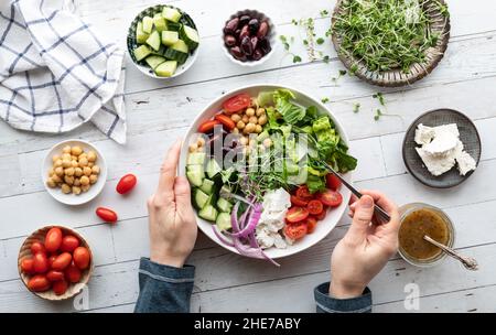 Vista dall'alto delle mani che tengono e mangiano da una ciotola di insalata greca appena fatta. Foto Stock