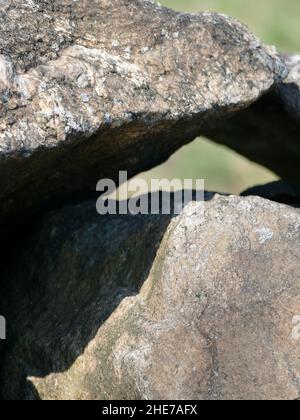 Una fotografia ravvicinata delle rocce grigie che si appoggiano e si equilibrano l'uno contro l'altro proiettando un'ombra in un giorno di primavera soleggiato con uno sfondo sfocato Foto Stock