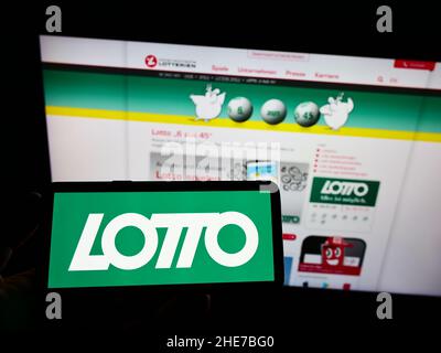 Persona che tiene uno smartphone con il logo della lotteria austriaca di Österreichische Lotterien GmbH sullo schermo di fronte al sito web. Mettere a fuoco sul display del telefono. Foto Stock