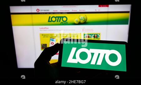 Persona che detiene il telefono cellulare con il logo della lotteria austriaca di Österreichische Lotterien GmbH sullo schermo di fronte al sito web. Mettere a fuoco sul display del telefono. Foto Stock