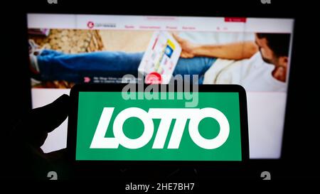 Persona che detiene il cellulare con il logo della lotteria austriaca di Österreichische Lotterien GmbH sullo schermo di fronte alla pagina web. Mettere a fuoco sul display del telefono. Foto Stock