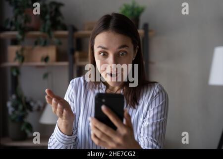 Shocked l'utente entusiasta dello smartphone che fissa lo schermo del telefono cellulare Foto Stock