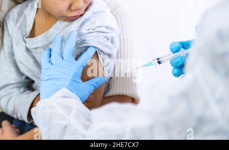 Una dottoressa che inietta il vaccino a un bambino con la madre. Vaccinazione dei bambini per l'immunizzazione nella pandemia di coronavirus, covid-19 Foto Stock