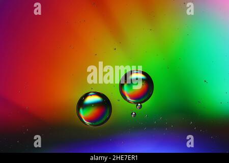 due gocce di olio galleggiano su una superficie d'acqua che brilla nei colori di un arcobaleno, primo piano Foto Stock