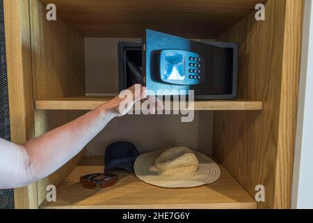 L'uomo apre la porta della cassaforte che siede sullo scaffale nell'armadio della camera d'albergo. Foto Stock