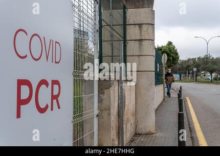 Primo piano di un poster della PCR Covid all'esterno di un centro di vaccinazione. Sullo sfondo, fuori fuoco, un uomo che indossa una maschera facciale Foto Stock