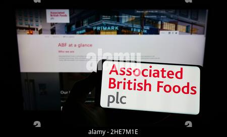 Persona che tiene uno smartphone con il logo della società Associated British Foods plc (ABF) sullo schermo di fronte al sito web. Mettere a fuoco sul display del telefono. Foto Stock