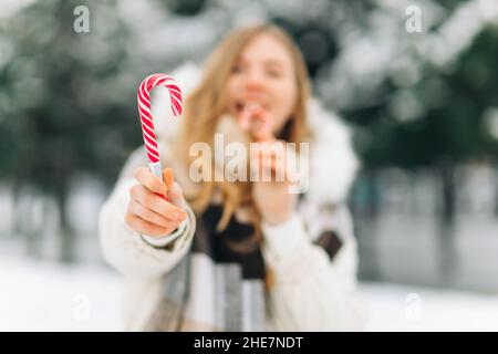 Ritratto di strada di bella donna sorridente felice posa all'aperto con caramelle rosse di Natale, modello indossando abiti caldi ed eleganti. Nevicate magiche. Chris Foto Stock