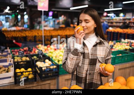 Cliente femminile che puzzava di arancia in un supermercato. La donna sceglie le arance. Ragazza al reparto frutta di un negozio di alimentari Foto Stock
