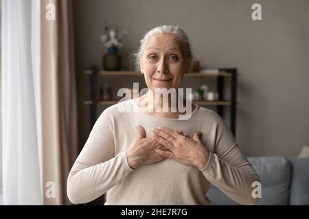 Sorridente donna di mezza età che tiene le mani piegate sul petto. Foto Stock