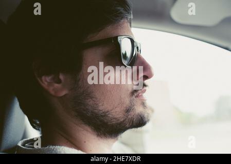 Uomo con occhiali da sole al volante che guida un'auto. Foto Stock