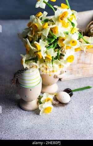 Carta floreale di Pasqua con fiori di daffodil in scatola di legno con uova colorate su sfondo di cemento Foto Stock