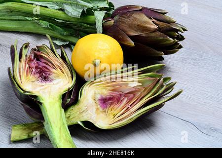 Carciofi su sfondo grigio di legno con limone. Foto Stock