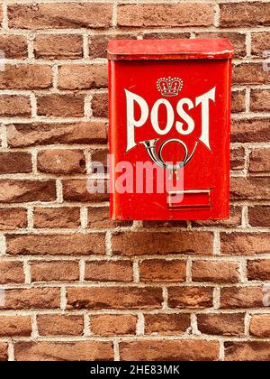 Tradizionale vecchia casella di posta in metallo rosso brillante con parola e foto di corno sulla parte anteriore attaccato alla facciata della casa, vecchia parete di mattoni di casa. Servizio postale p Foto Stock