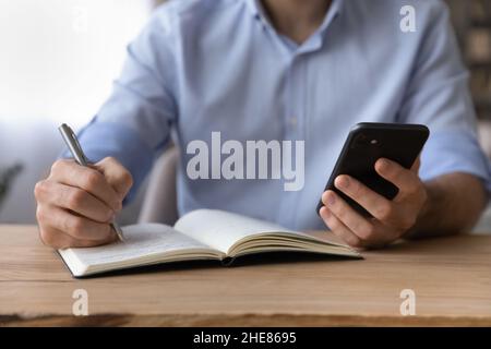 Primo piano ritagliato uomo d'affari con smartphone, annotando le informazioni Foto Stock