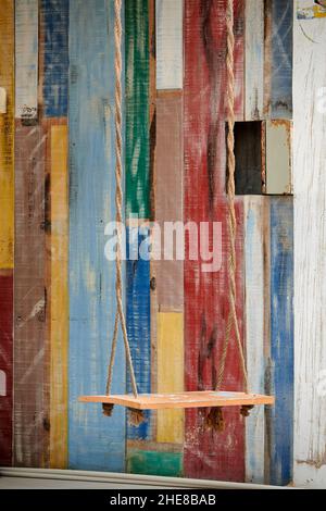 La corda vuota del banco oscilla contro un muro colorato di legno a strisce a Isla Holbox, Messico Foto Stock