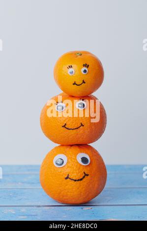 Pila di tre tangerini con facce divertenti contro sfondo bianco e blu Foto Stock