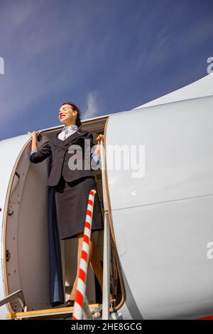Donna allegra stewardess in piedi nella porta dell'aeroplano Foto Stock