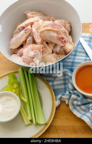 Ali di pollo crude fresche con salsa calda, salsa di formaggio blu e sedano su un tagliere di legno in una cucina casalinga Foto Stock