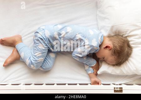 Vista dall'alto cute Little 2-3 anni prescolare bambino ragazzo bambino dormire dolcemente in culla bianca durante il pranzo riposo in pajama blu con cuscino a casa Foto Stock