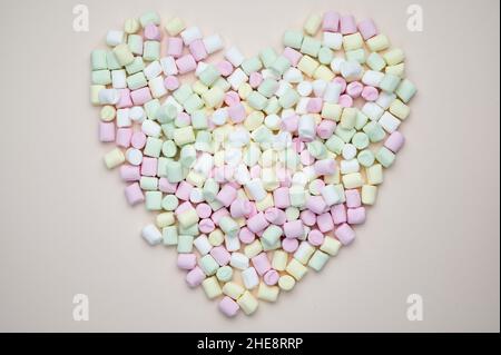 Le marshmallows in colori luminosi giacciono a forma di cuore su sfondo pastello Foto Stock