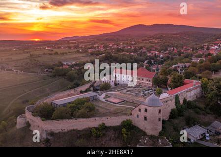 Scatto aereo al tramonto della chiesa fortificata di Pecsvarad e del castello con torre, porta sulla cima di una collina nella contea di Baranya Ungheria Foto Stock