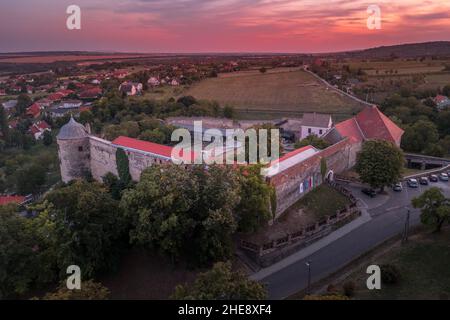 Scatto aereo al tramonto della chiesa fortificata di Pecsvarad e del castello con torre, porta sulla cima di una collina nella contea di Baranya Ungheria Foto Stock