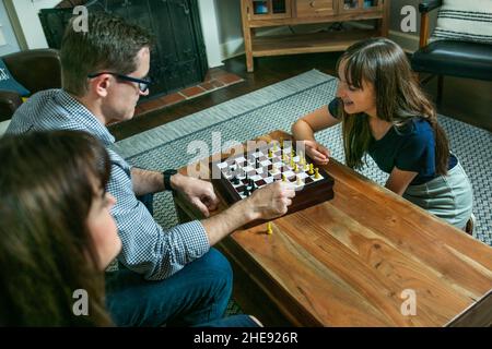 Una famiglia di tre persone con una madre e un padre e una figlia seduta su un divano e giocare a scacchi per la competizione notturna di gioco di famiglia Foto Stock
