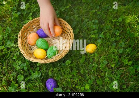 Caccia di Pasqua. Raccolta uova di Pasqua. Il bambino raccoglie le uova e mette in un cestino nel giardino primaverile.uova di pasqua colorate. Festa religiosa Foto Stock