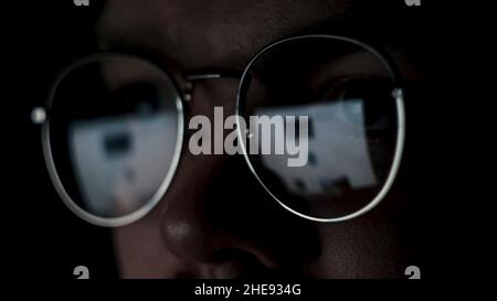 Primo piano degli occhi di un uomo con occhiali al computer isolato su sfondo nero. Il riflesso dello schermo negli occhiali di un genio o ne Foto Stock