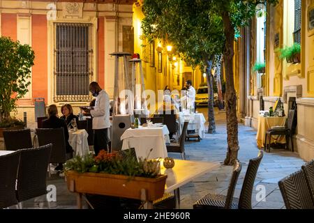 I camerieri e i server indossano maschere per proteggere i clienti e i clienti dal virus Covid di notte in un ristorante all'aperto a Siviglia, in Spagna. Foto Stock