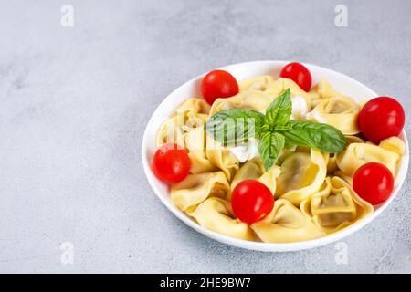 Ravioli con pomodoro e basilico su sfondo grigio. Ravioli freschi fatti in casa. Spazio copia Foto Stock