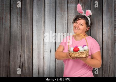 Donna in orecchie conigliate con uova di Pasqua in un cestino su sfondo di legno Foto Stock