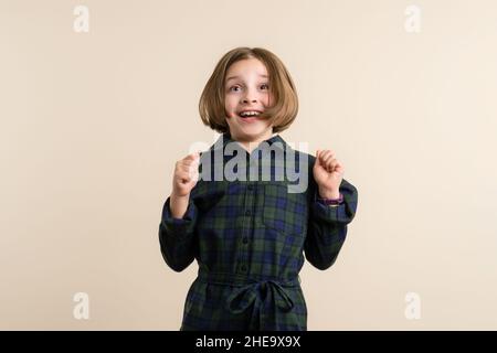 Eccitata Kid Little Girl 9s vestito con camicia a maglia Jump up. Primo piano interno portrair ottimista bambino grida di gioia Foto Stock