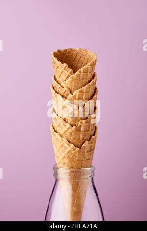 Svuotare i coni del gelato in una bottiglia di vetro con sfondo viola chiaro. Foto Stock