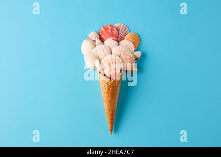 Design estivo con conchiglie colorate e cono gelato su sfondo blu. Cucina creativa e minimale sulla spiaggia con vista piatta. Foto Stock