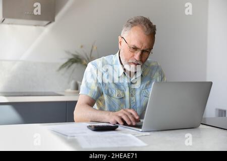 Uomo pensionato di mezza età concentrato che calcola il budget. Foto Stock