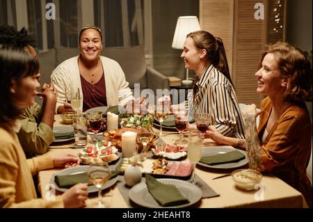 Gruppo di amici felici seduti al tavolo da pranzo che parlano e ridono l'uno con l'altro a cena partito a casa Foto Stock