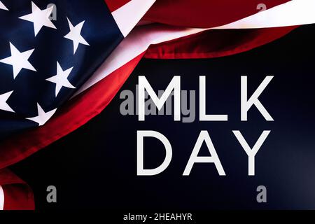 Sfondo nero e bandiera americana con testo abbreviato MLK. Disposizione piatta. Happy Martin Luther King Day Concept Foto Stock