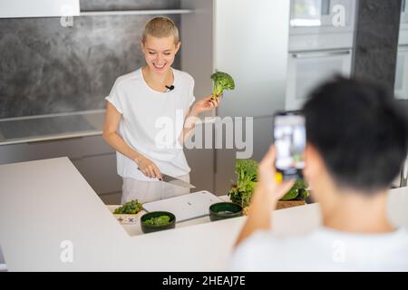 Uomo prendere video su smartphone di donna cuoco insalata Foto Stock
