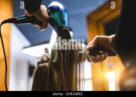 Master donna parrucchiere asciuga i capelli della ragazza con un asciugacapelli e pettini dopo il lavaggio nel salone di bellezza. Foto Stock