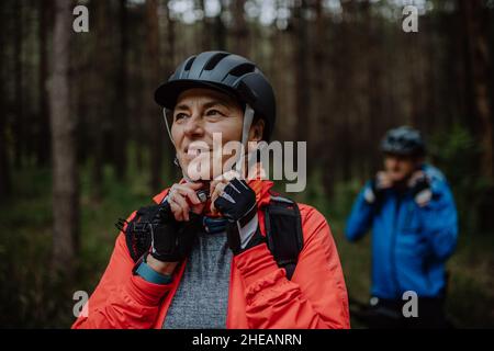 Motociclisti senior che mettono il casco da ciclismo all'aperto nella foresta nel giorno d'autunno. Foto Stock