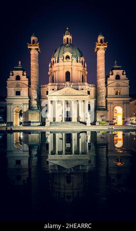 Immagine verticale della chiesa di Karslkirche e dei suoi reflectios di notte con turisti seduti nelle vicinanze. Toruismo ed edifici storici a Viena Foto Stock