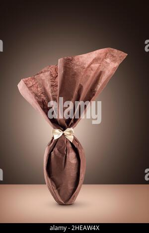 Uovo di pasqua al cioccolato confezionato con elegante carta marrone su sfondo marrone Foto Stock