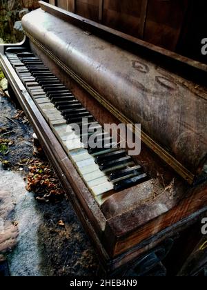 Pianoforte abbandonato con chiavi intemprate e uno strato di polvere, riposante in un ambiente rustico all'aperto circondato dalla natura, evidenziando il decadimento e l'oblio Foto Stock