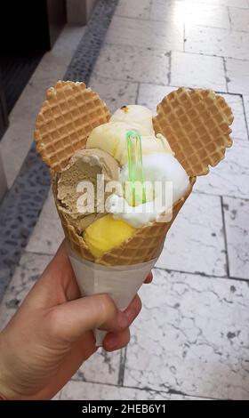 Morsi il cono gelato in mano. In forma di palline multicolore con orecchie Foto Stock