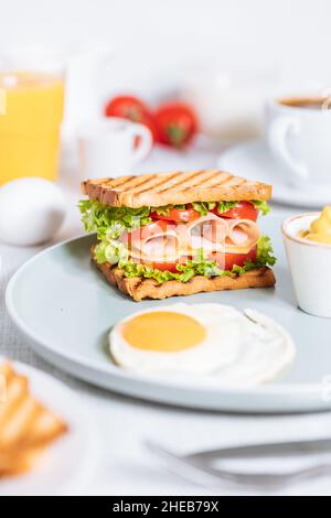 Toast sandwich con formaggio gouda e prosciutto di tacchino ripieno di pomodoro e lattuga su uno sfondo luminoso con ingredienti in sfondo sfocato. Wi servito Foto Stock